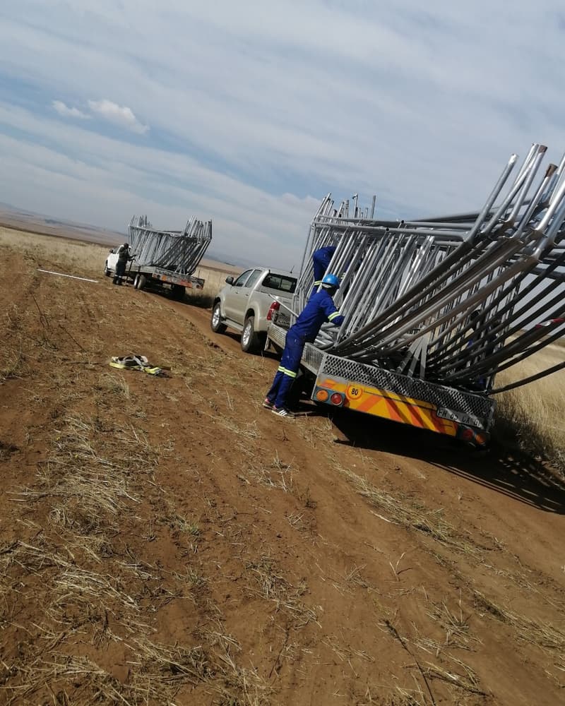 Installers unloading steel arches from trailers on a farm road
