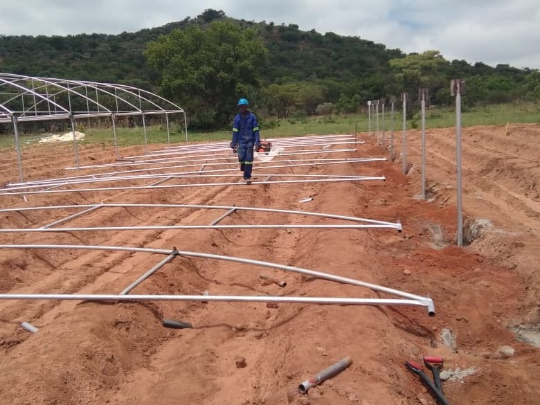 Installer walking across a pegged-out site with steel base rails laid on red soil