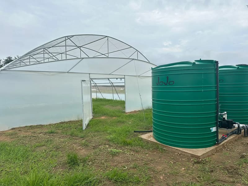 Two white polythene tunnels side by side with green water tanks beside them