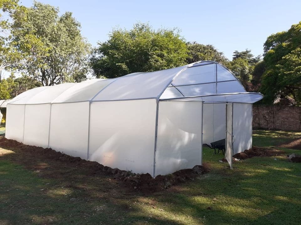 Hobby tunnel covered in white plastic in a garden, with its gable flap raised